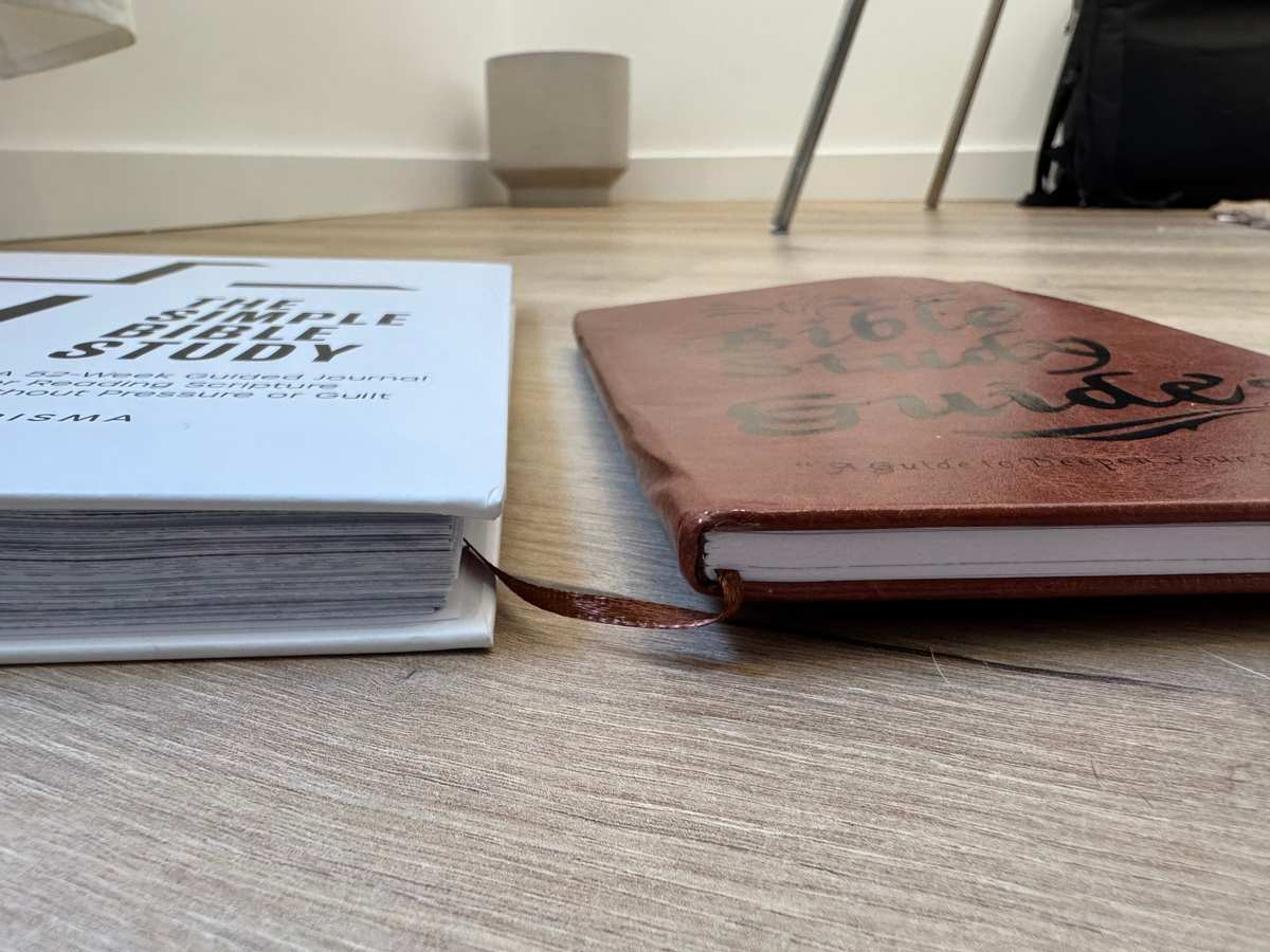 Side profile comparison showing The Simple Bible Study by Everisma is significantly thicker with a hardcover and gold spiral binding next to the much thinner Elvasma Bible Study Guide on a hardwood floor