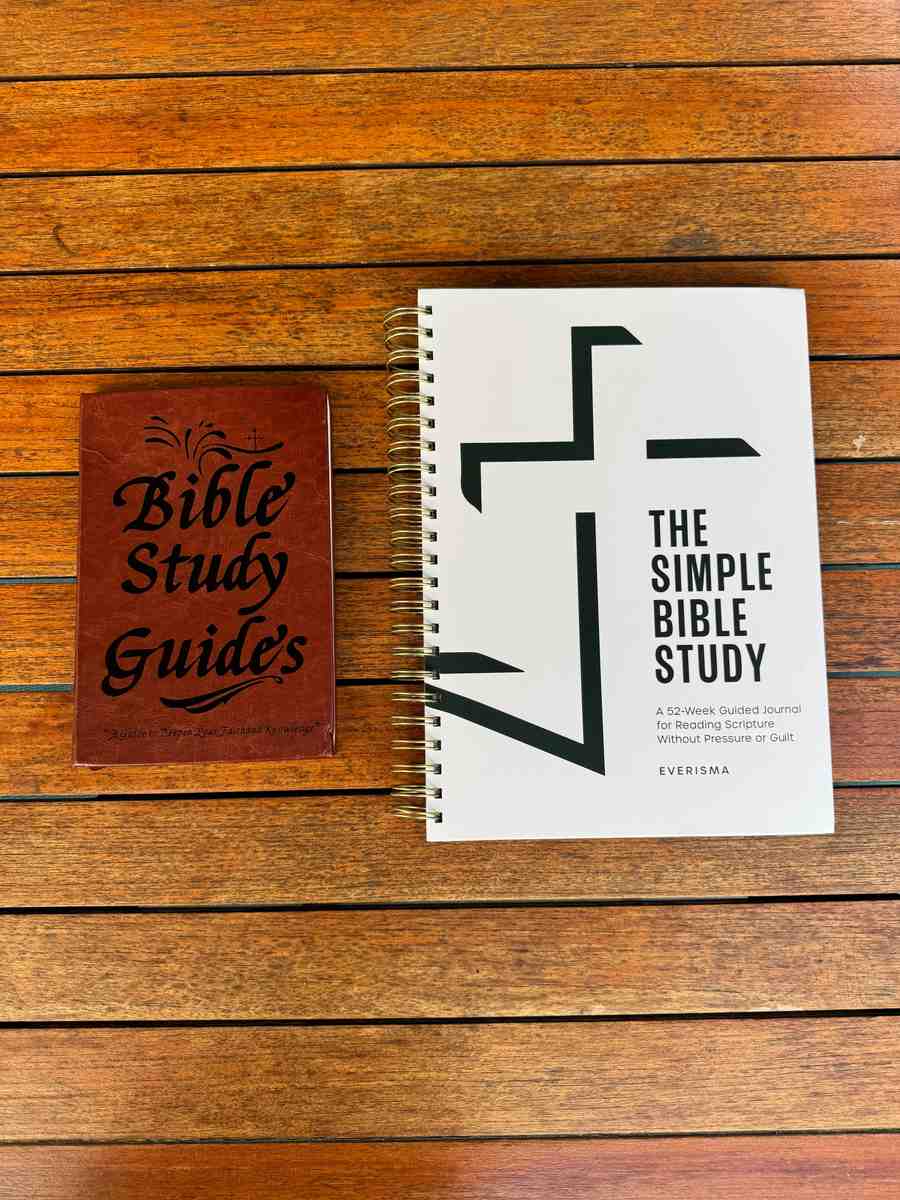 Top-down view of the Elvasma Bible Study Guide and The Simple Bible Study by Everisma laid flat on a wood table, showing the difference in size, format, and design between the two Bible study guides